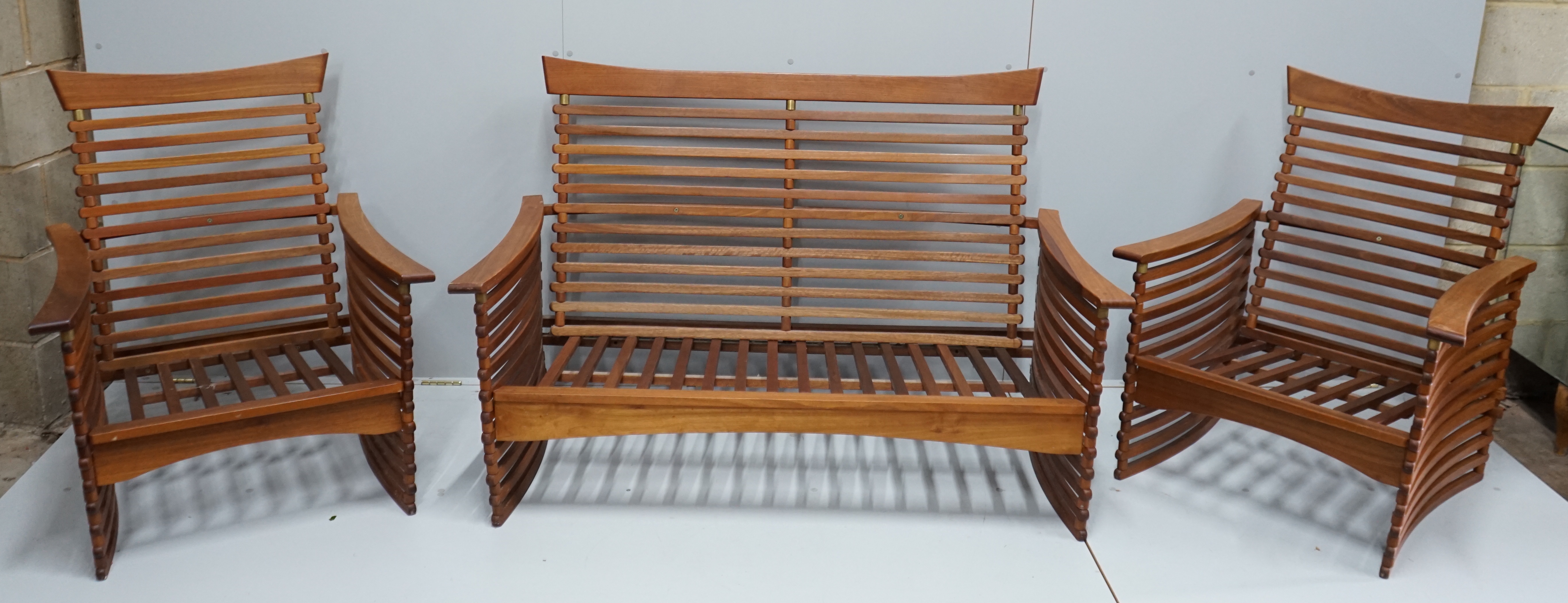 In the manner of Finn Juhl, a Danish brass mounted teak three piece lounge suite of slatted form, settee width 143cm, depth 77cm, height 92cm.